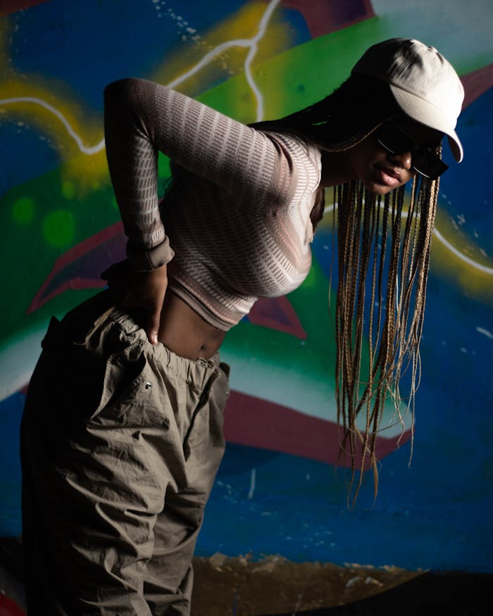 Stylish woman with dreadlocks poses against colorful urban graffiti backdrop, embodying casual street fashion.