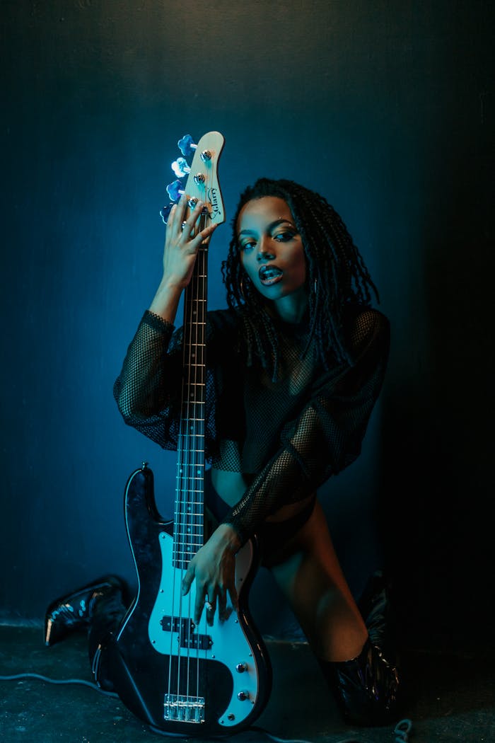 A black woman kneeling with an electric guitar in dramatic lighting.