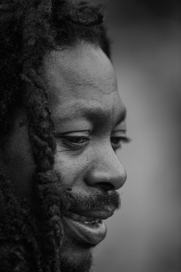 Monochrome close-up portrait of a man with facial hair and dreadlocks.